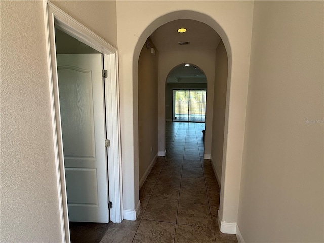 corridor featuring dark tile patterned flooring, baseboards, visible vents, and arched walkways