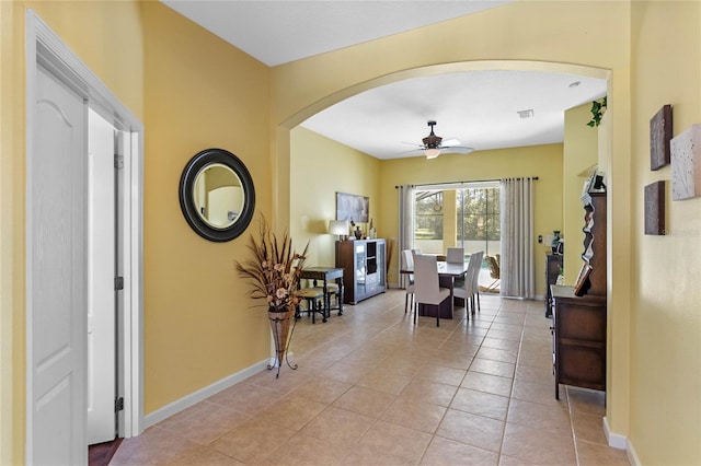 dining space with arched walkways, light tile patterned floors, visible vents, a ceiling fan, and baseboards