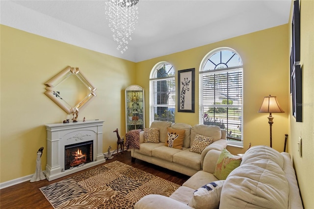 living area with a warm lit fireplace, a chandelier, wood finished floors, and baseboards