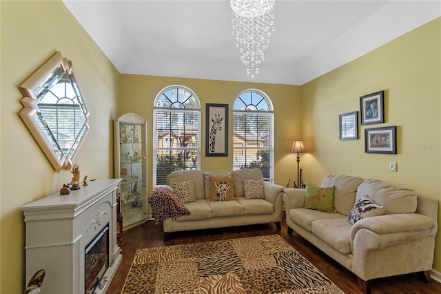 living area featuring dark wood-style floors, a glass covered fireplace, and a notable chandelier