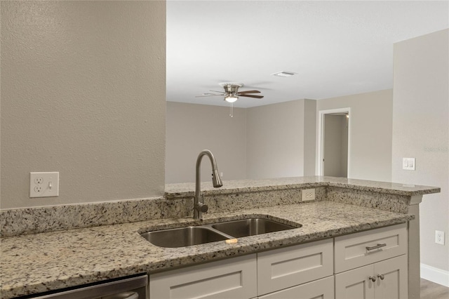 kitchen featuring light stone counters, white cabinets, a sink, and dishwasher