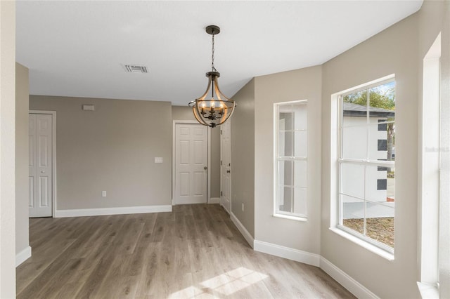 unfurnished dining area featuring light wood-style floors, a chandelier, visible vents, and baseboards