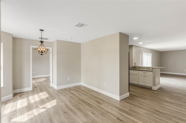 empty room with a chandelier, light wood-style flooring, a sink, visible vents, and baseboards