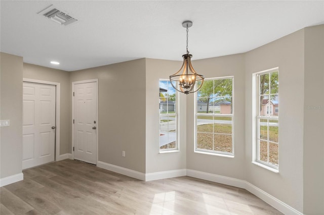 unfurnished dining area with light wood finished floors, baseboards, visible vents, and a notable chandelier