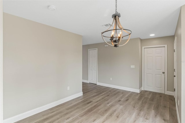 empty room featuring light wood finished floors, an inviting chandelier, visible vents, and baseboards