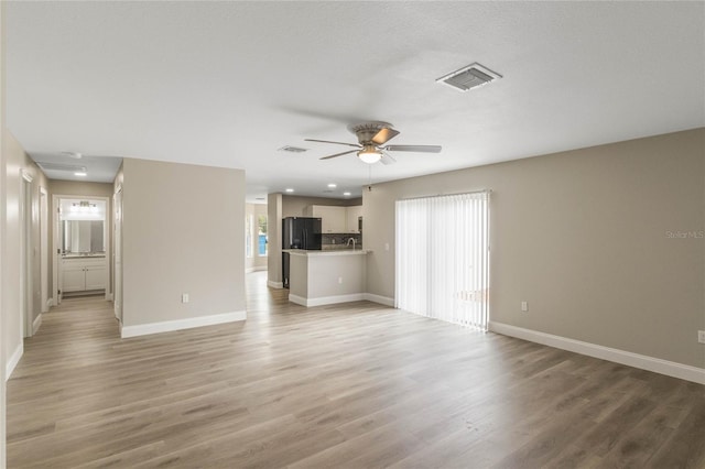 unfurnished living room featuring light wood-type flooring, ceiling fan, visible vents, and baseboards