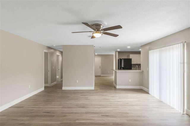 unfurnished living room with ceiling fan, light wood-style flooring, and baseboards