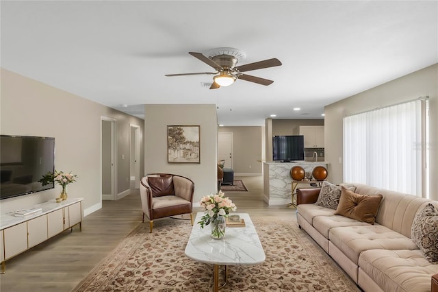 living room with light wood-type flooring, baseboards, and a ceiling fan