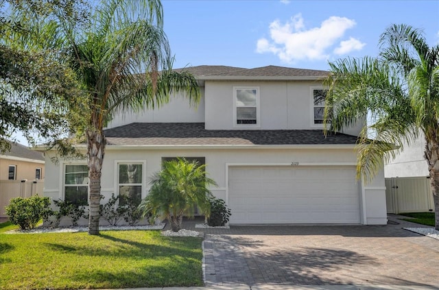 view of front of house featuring an attached garage, a shingled roof, decorative driveway, stucco siding, and a front lawn