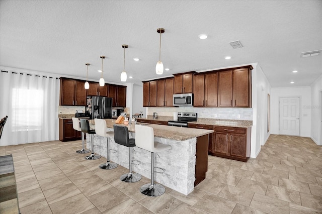 kitchen with decorative light fixtures, visible vents, appliances with stainless steel finishes, a kitchen bar, and a center island with sink