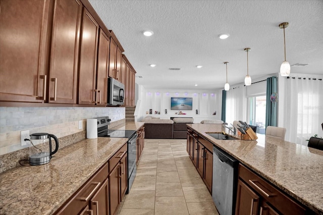 kitchen with light stone countertops, appliances with stainless steel finishes, open floor plan, and a sink