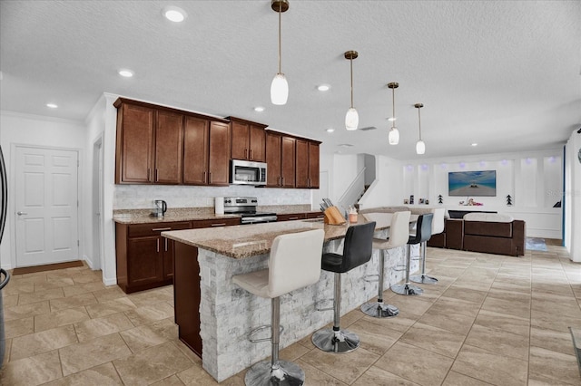 kitchen with recessed lighting, a breakfast bar, hanging light fixtures, appliances with stainless steel finishes, and light stone countertops