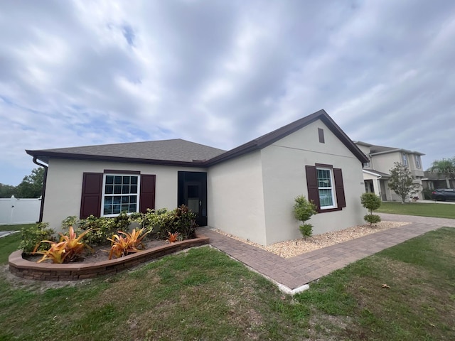 view of front of home with stucco siding, a front yard, and fence