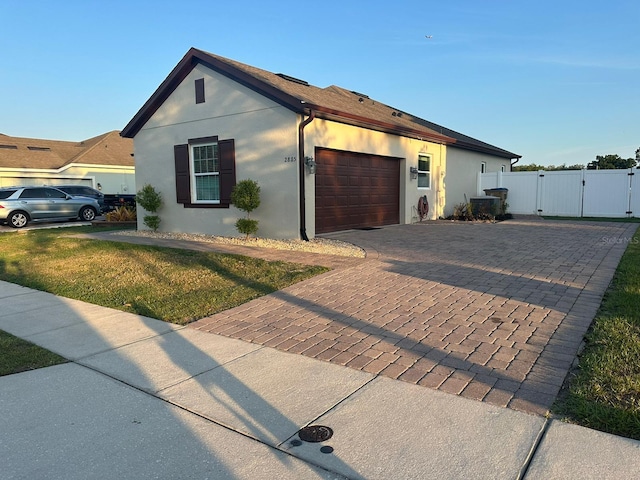 view of side of home with decorative driveway, a gate, an attached garage, and stucco siding