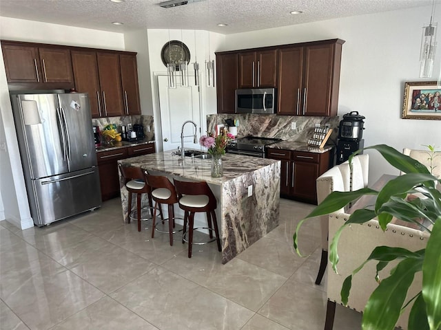 kitchen with a sink, appliances with stainless steel finishes, dark stone counters, a kitchen bar, and a center island with sink