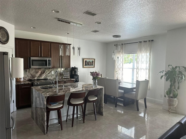 kitchen with visible vents, backsplash, appliances with stainless steel finishes, dark stone counters, and a kitchen bar