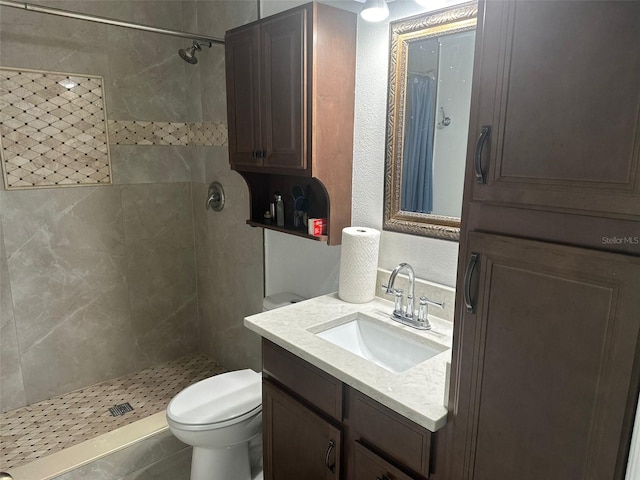 bathroom featuring toilet, tiled shower, and vanity