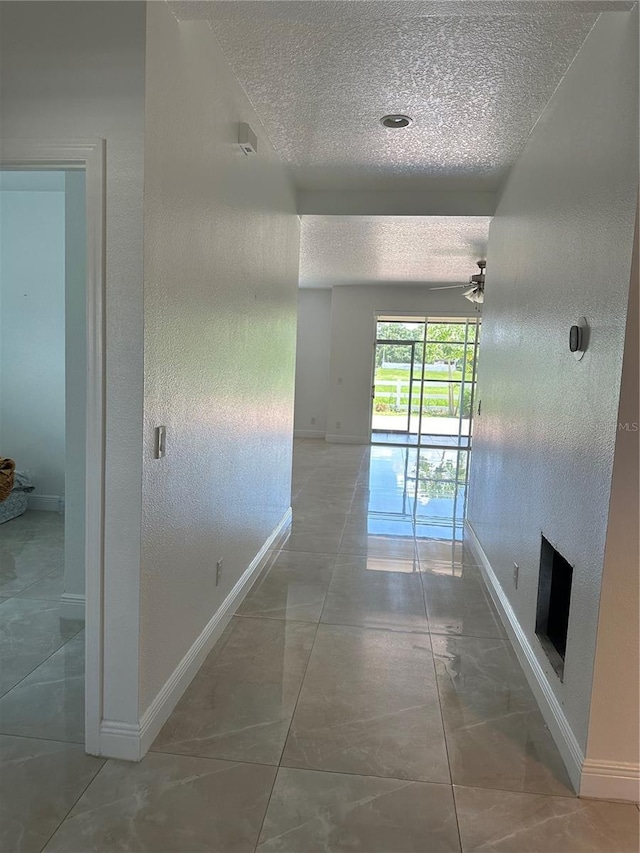 hallway with a textured ceiling, marble finish floor, a textured wall, and baseboards