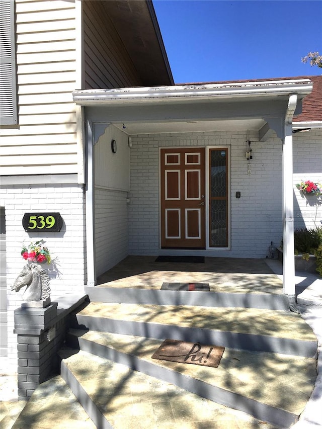 view of exterior entry featuring covered porch and brick siding