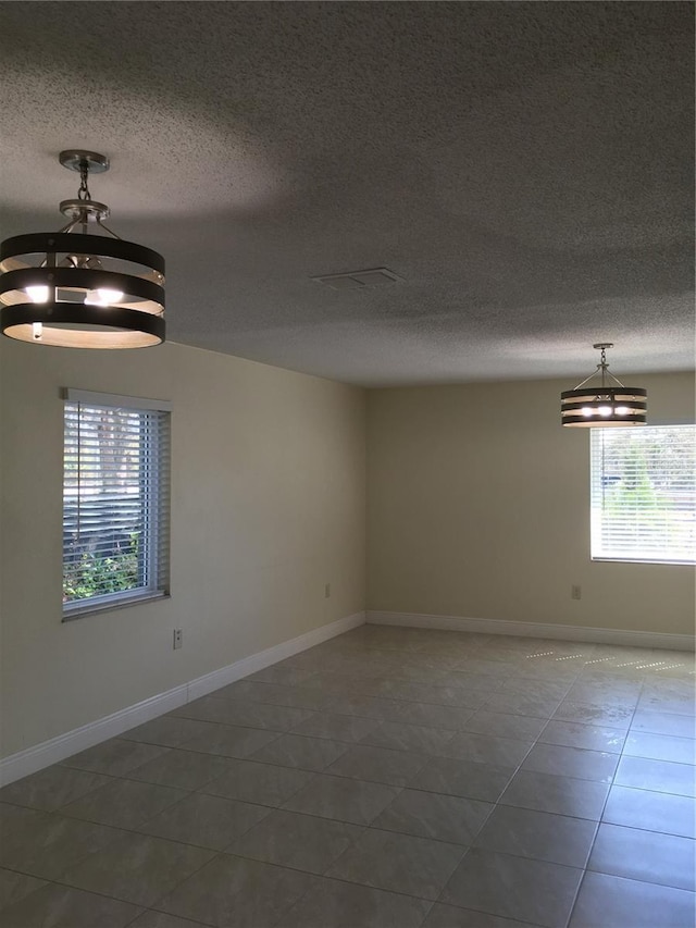 empty room with a textured ceiling, baseboards, and tile patterned floors