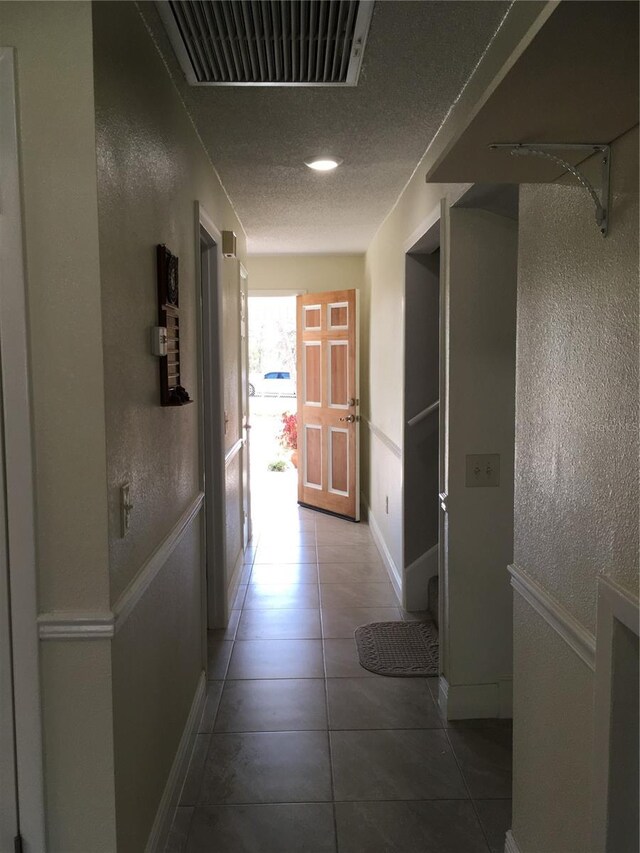 corridor featuring a textured ceiling, a textured wall, tile patterned flooring, and visible vents