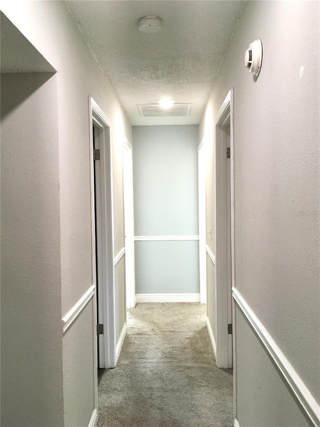 hallway with a textured ceiling, carpet floors, and baseboards