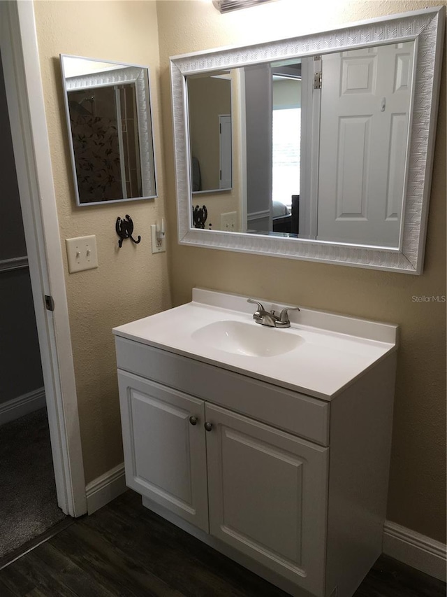 bathroom with a textured wall, vanity, baseboards, and wood finished floors