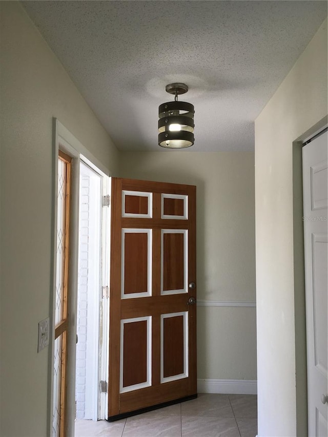 hallway with a textured ceiling, light tile patterned flooring, and baseboards