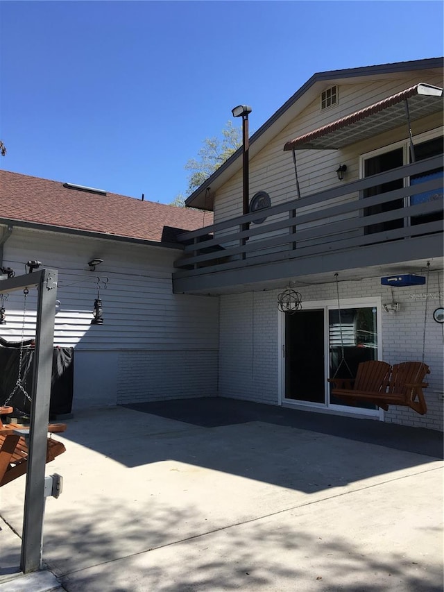 exterior space featuring a patio area, brick siding, and roof with shingles