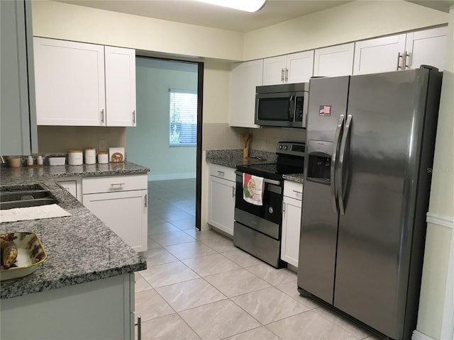 kitchen featuring light tile patterned floors, stainless steel appliances, white cabinetry, a sink, and dark stone counters