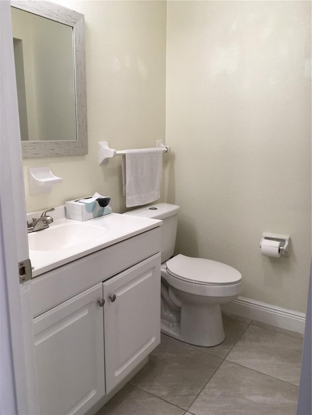 half bathroom featuring toilet, tile patterned flooring, baseboards, and vanity