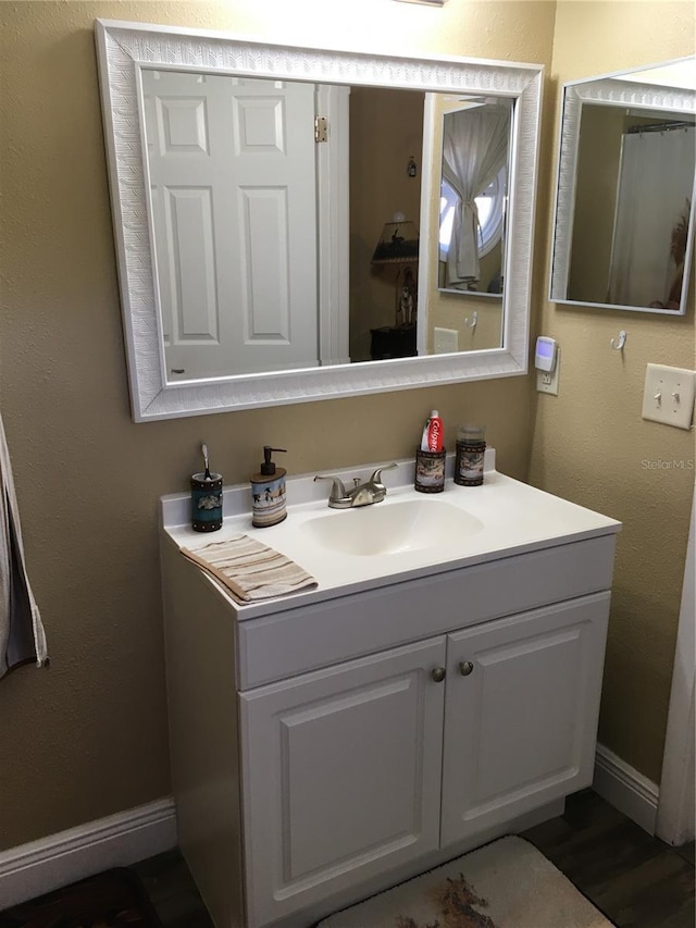 bathroom featuring a textured wall, baseboards, wood finished floors, and vanity