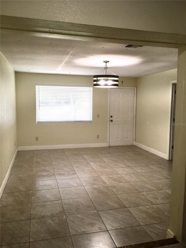 empty room featuring baseboards, visible vents, and tile patterned flooring