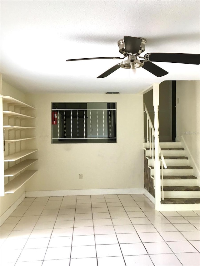 tiled empty room with a ceiling fan, visible vents, stairway, and baseboards
