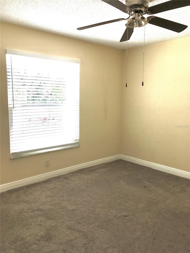 empty room featuring a ceiling fan, dark carpet, and baseboards