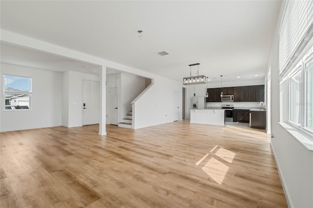 unfurnished living room with visible vents, baseboards, stairway, light wood-style floors, and a sink