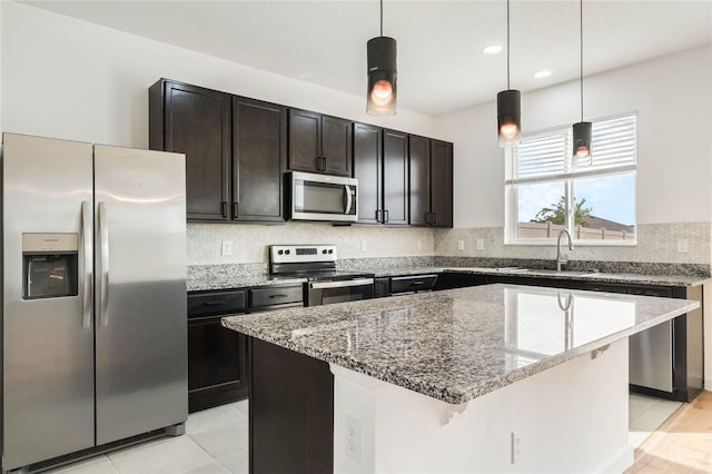 kitchen with a center island, stainless steel appliances, tasteful backsplash, a sink, and light stone countertops