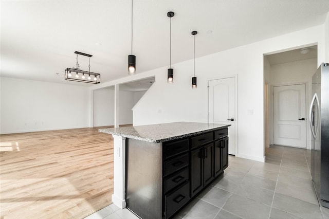 kitchen featuring a kitchen island, dark cabinets, decorative light fixtures, freestanding refrigerator, and light stone countertops