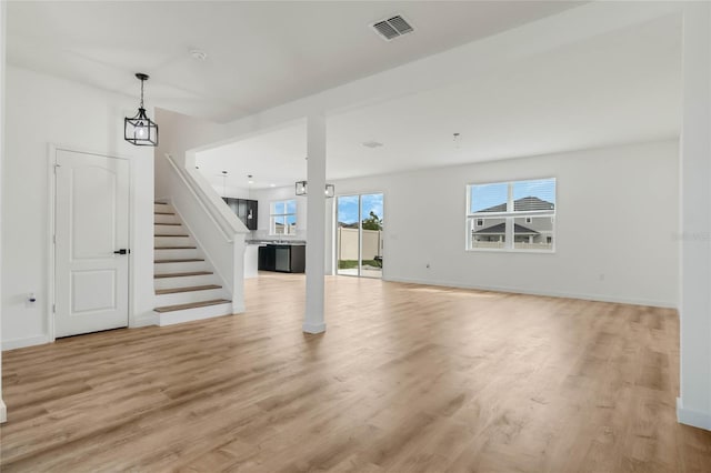 unfurnished living room featuring light wood-style floors, visible vents, baseboards, and stairs