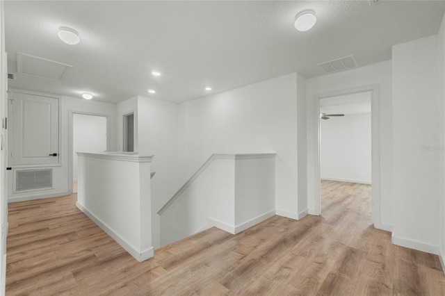 hall with visible vents, light wood-style floors, an upstairs landing, and attic access