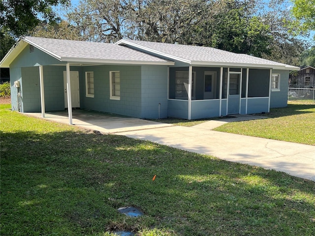 ranch-style home featuring a sunroom, a front yard, concrete block siding, and roof with shingles