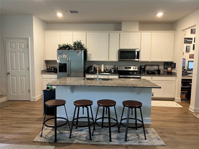 kitchen featuring wood finished floors, a sink, white cabinetry, appliances with stainless steel finishes, and an island with sink