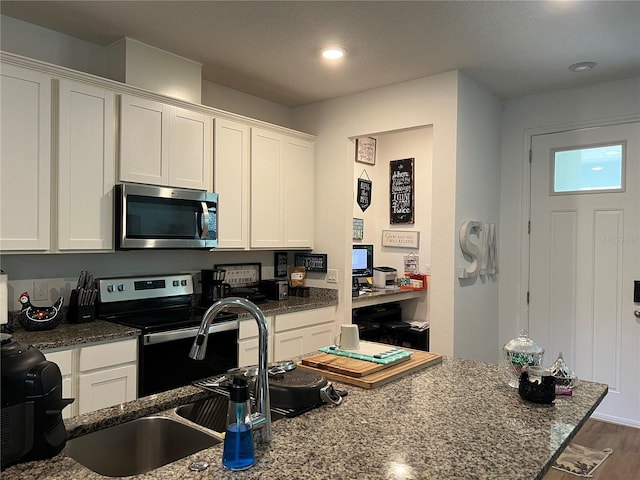 kitchen featuring appliances with stainless steel finishes, white cabinets, wood finished floors, and dark stone counters