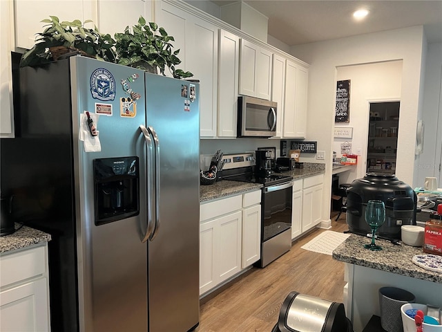 kitchen with stainless steel appliances, light wood-type flooring, stone counters, and white cabinets