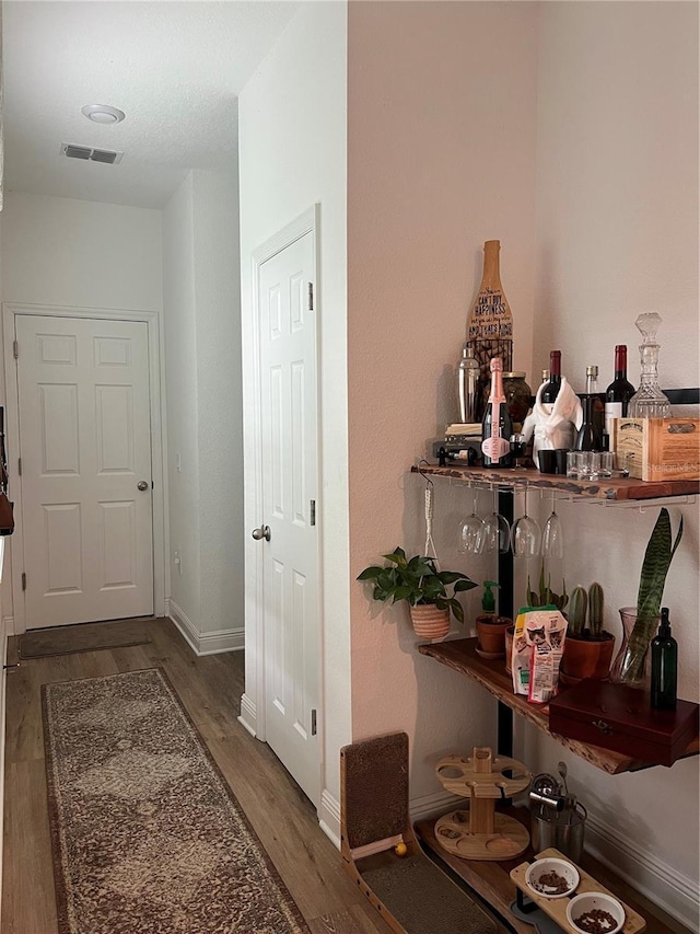 hallway with baseboards, visible vents, and wood finished floors