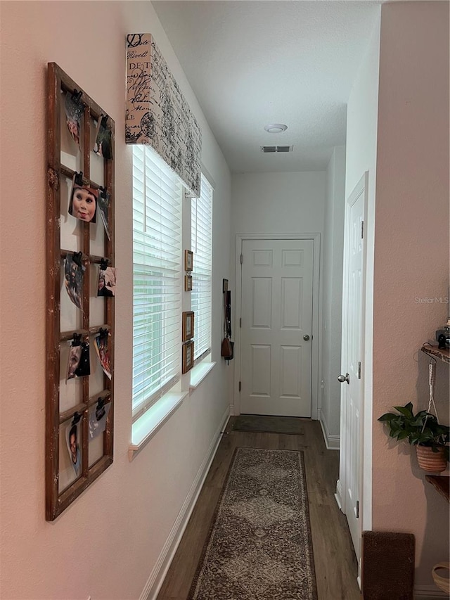 hall featuring visible vents, baseboards, and wood finished floors