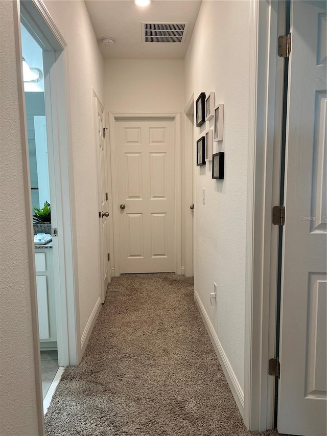 hall with carpet, visible vents, and baseboards