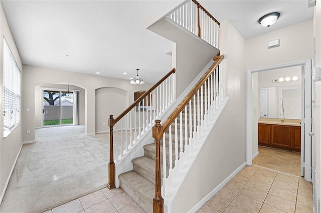 staircase featuring arched walkways, tile patterned flooring, carpet flooring, baseboards, and an inviting chandelier