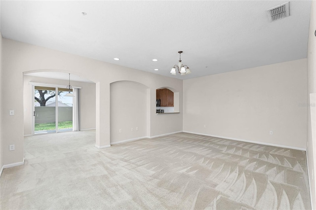 unfurnished living room with a chandelier, arched walkways, light carpet, visible vents, and baseboards