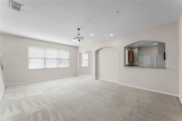 unfurnished living room featuring recessed lighting, visible vents, light carpet, a textured ceiling, and baseboards